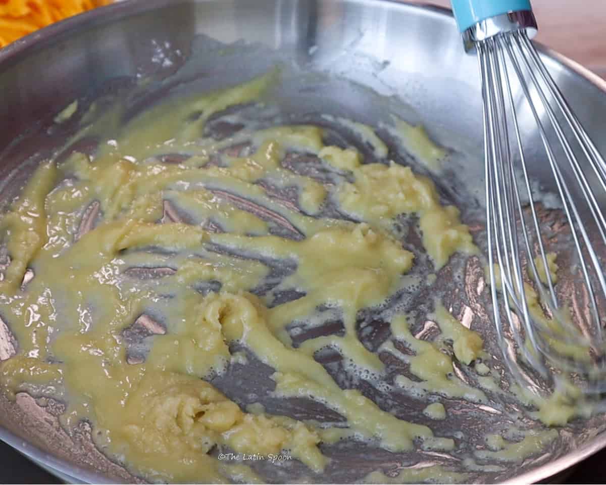 A skillet with a mixture of butter and flour being stirred with a whisk.