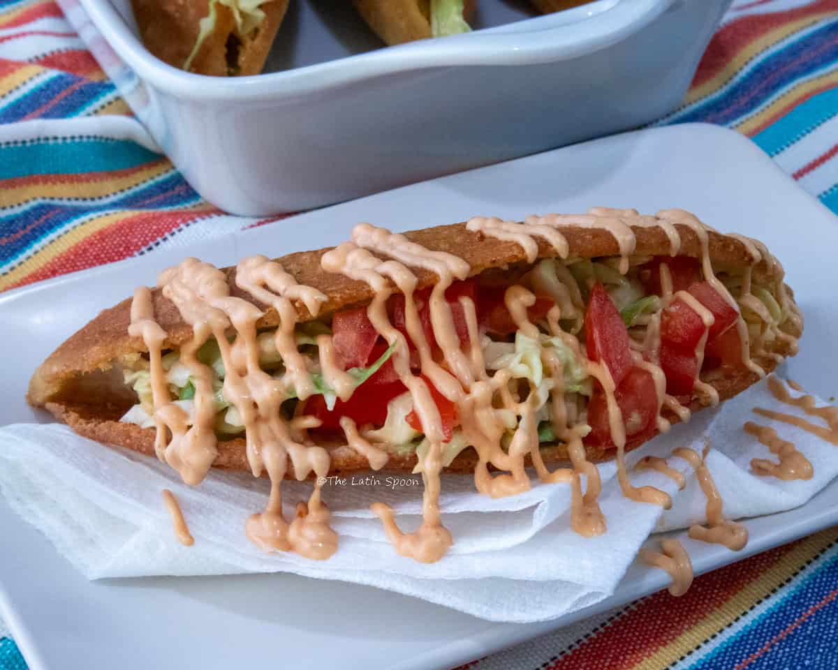 Three chicken empanadas opened along the side and filled with shredded cabbage and diced tomato, served with pink sauce on a white plate over a colorful tablecloth.