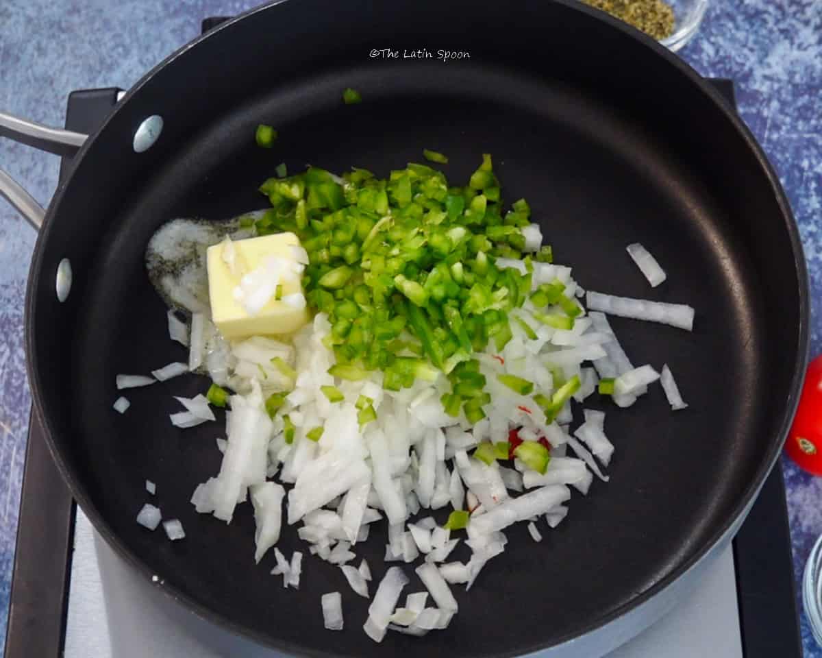 A skillet with chopped onion, bell pepper, celery, and butter.
