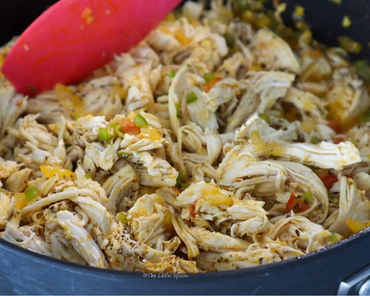 A skillet with seasoned shredded chicken being stirred with a spatula.