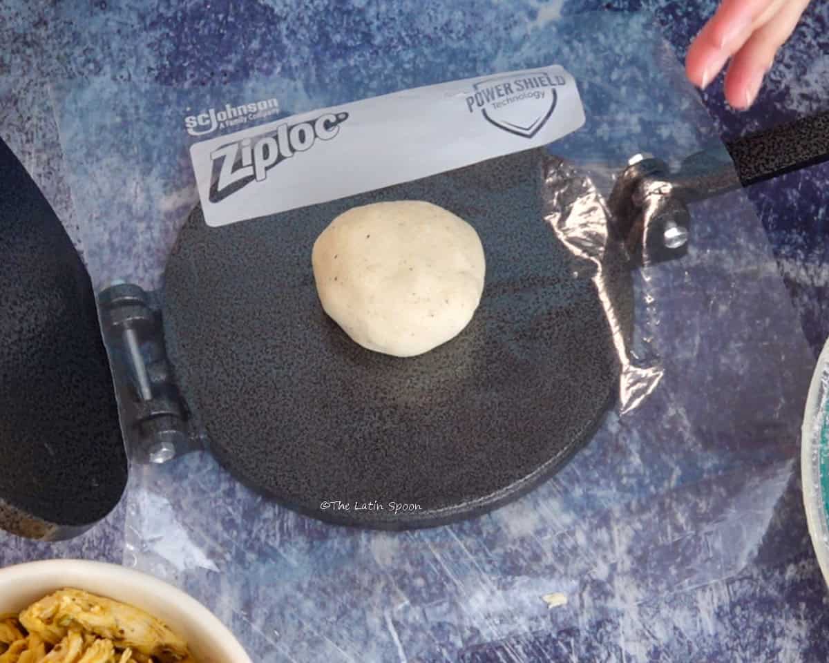 A ball of masa placed between plastic sheets in a tortilla press.