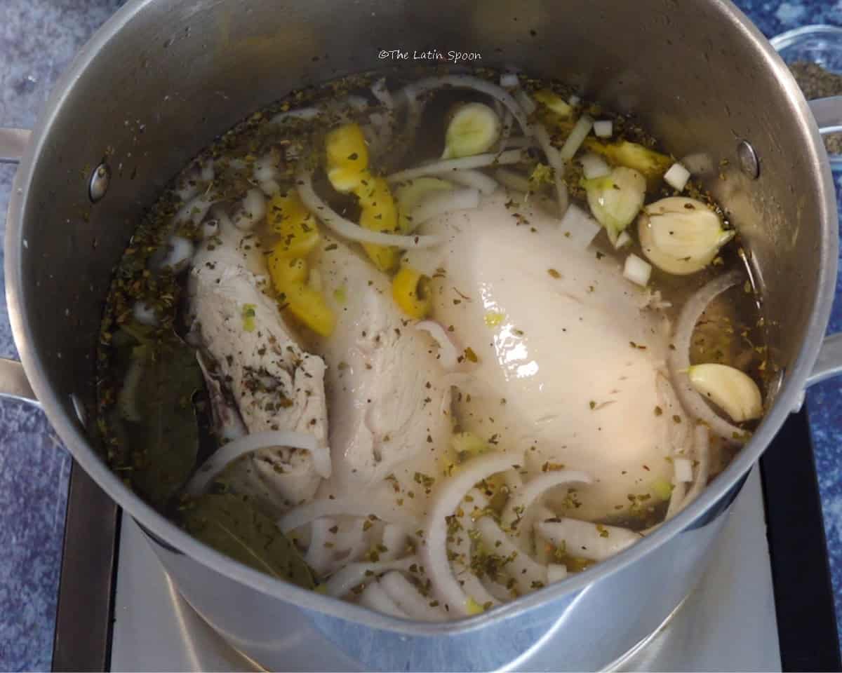 A pot with chicken breasts cooking in water with garlic, pieces of bell pepper, onion, and celery.