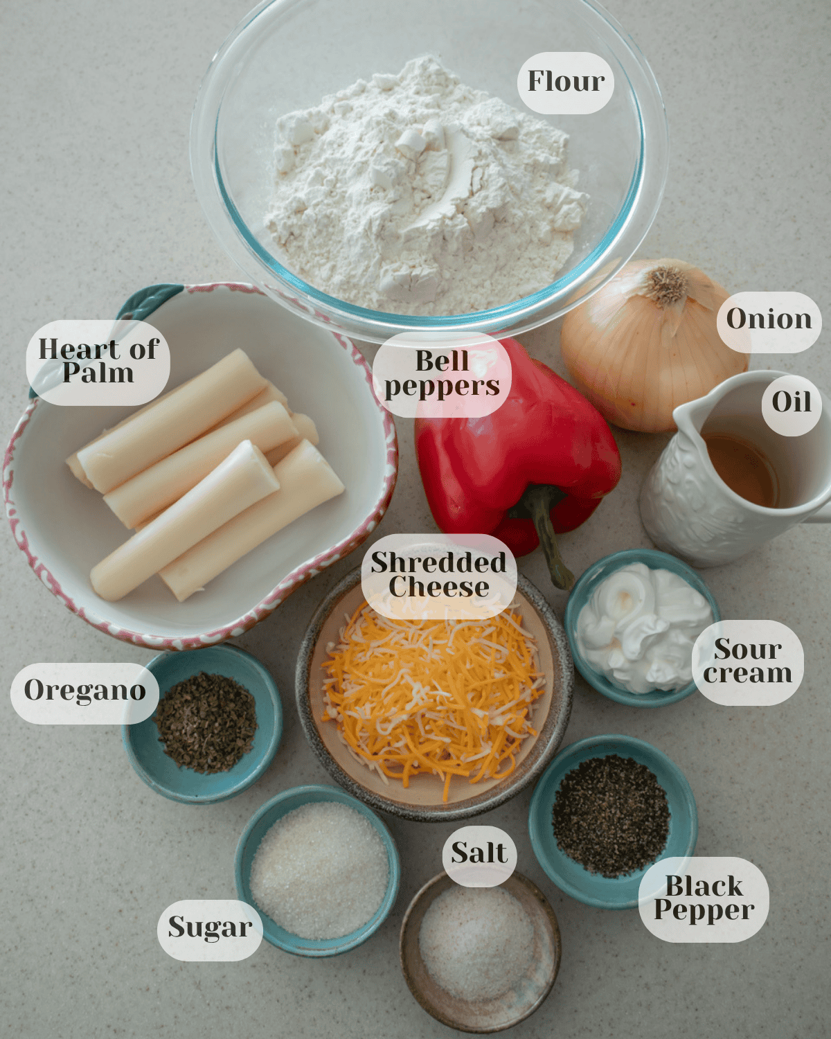 Ingredients arranged together: a cup of flour, hearts of palm, oil, grated cheese, oregano, cream cheese, black pepper, salt, sugar, a whole red bell pepper, and a whole onion.