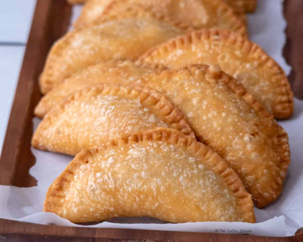 Eight empanadas arranged on wax paper over a wooden board.