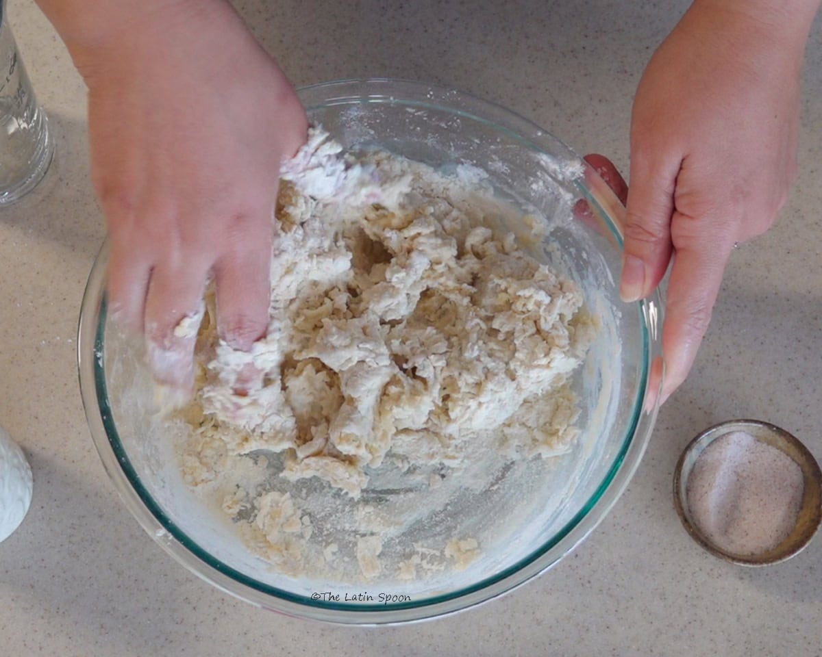 A glass bowl with one hand mixing the ingredients while the other hand holds the bowl steady.