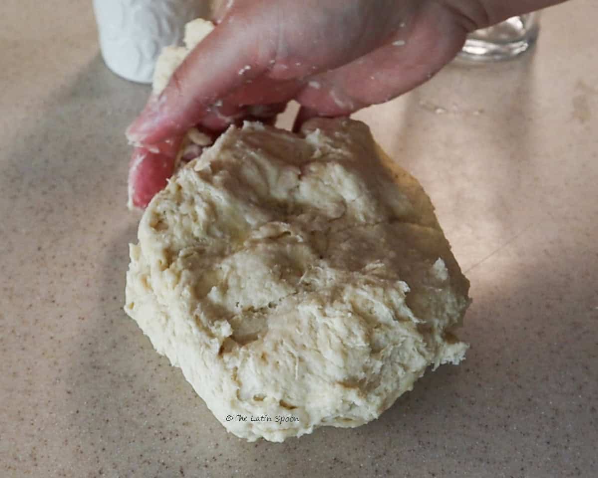 A ball of dough resting on a countertop and held with one hand.
