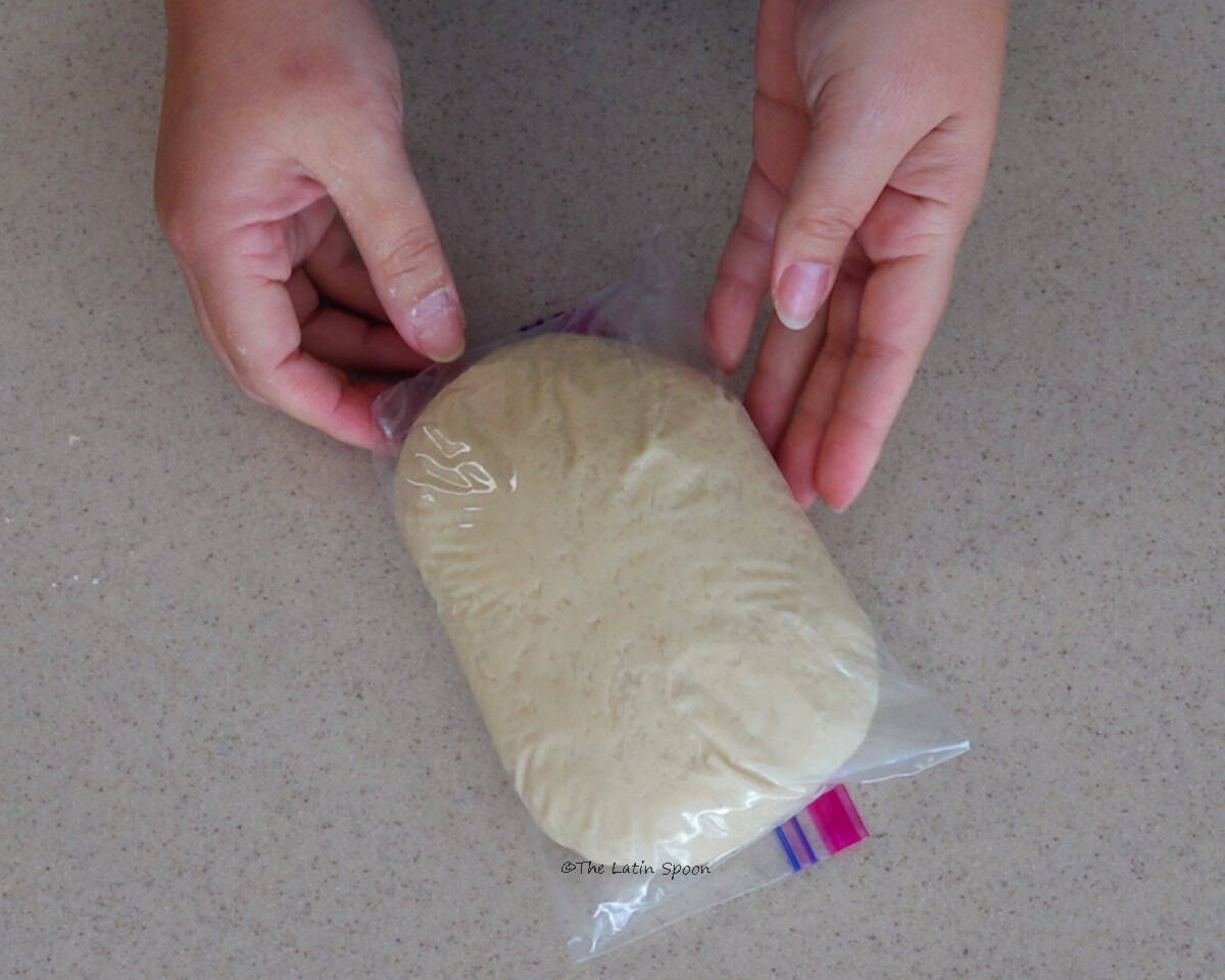 A plastic bag filled with dough, held with both hands.