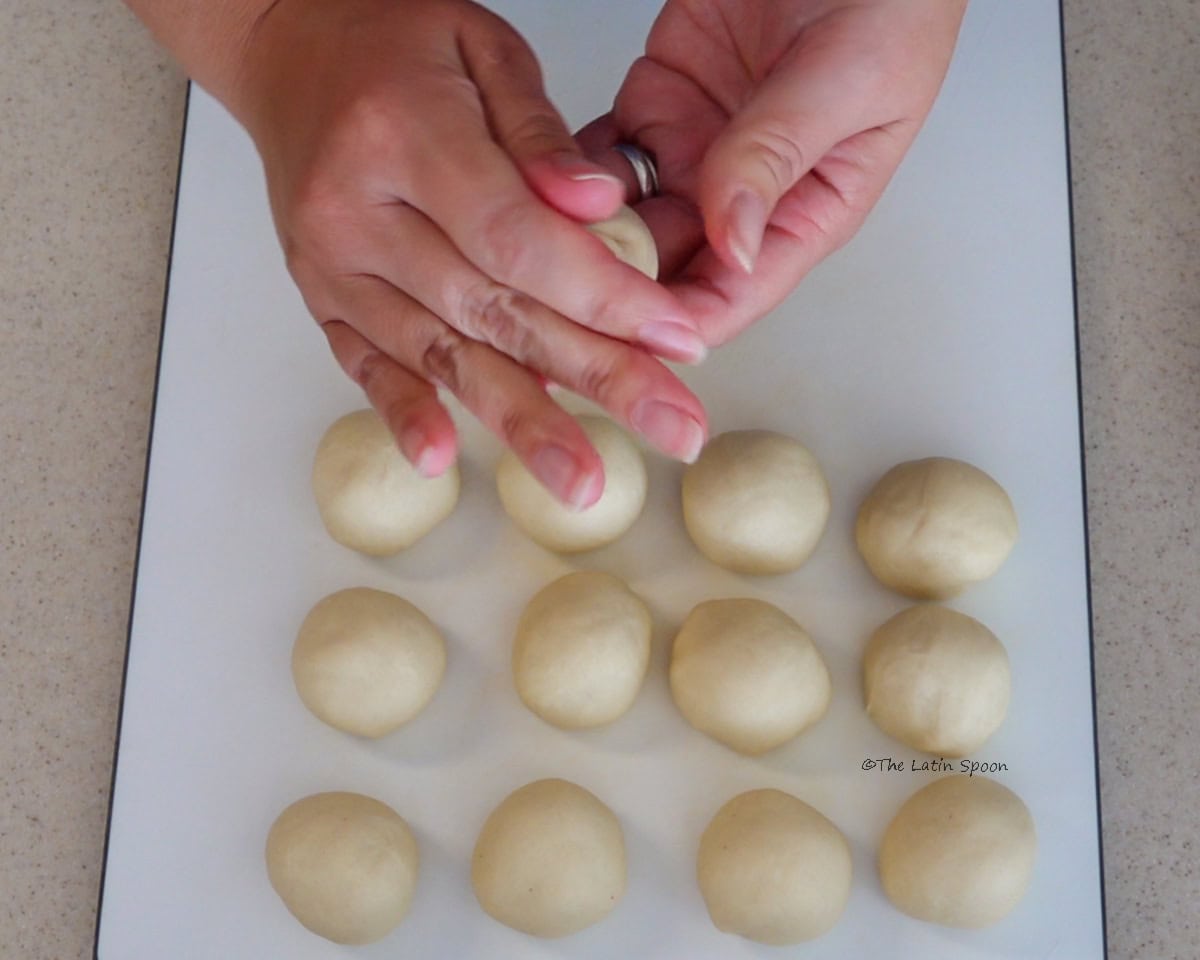 Two hands shaping the dough, with the finished dough balls resting on a cutting board.