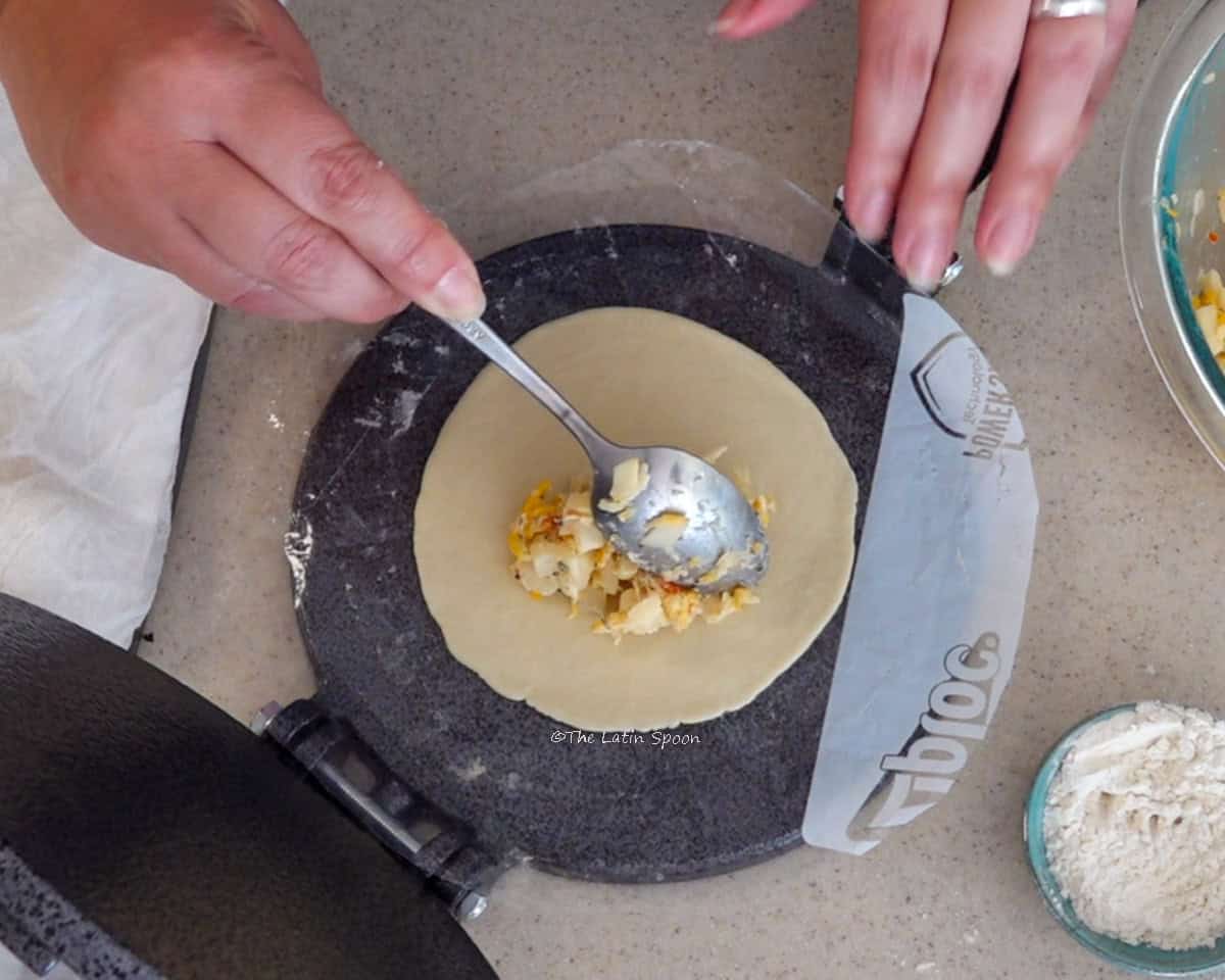 A spoonful of heart of palm mixture being placed onto the flattened dough while it rests on the tortilla press.