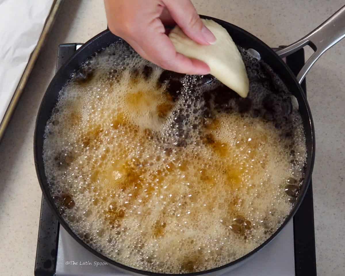 A hand carefully places the uncooked empanadas into a skillet filled with hot oil.