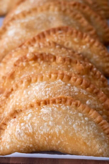 A heart of palm empanada cut in half, with other empanadas softly blurred in the background.