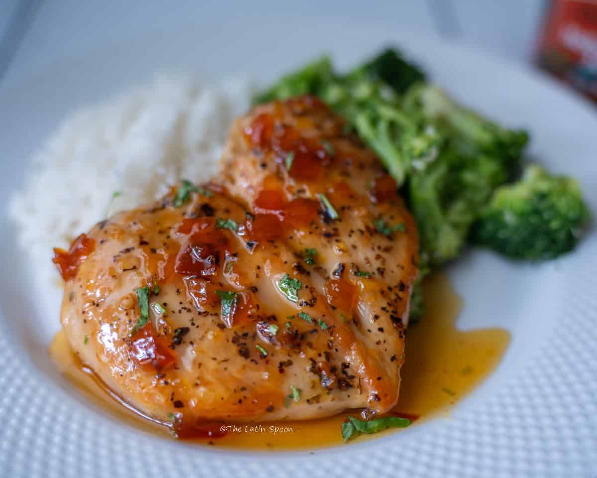 A white plate with rice served in the background, broccoli on the right, and jam-glazed chicken in the center. The jam and small pieces of cilantro can be seen on top of the chicken.
