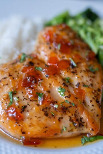 A white plate with rice served in the background, broccoli on the right, and jam-glazed chicken in the center. The jam and small pieces of cilantro can be seen on top of the chicken.