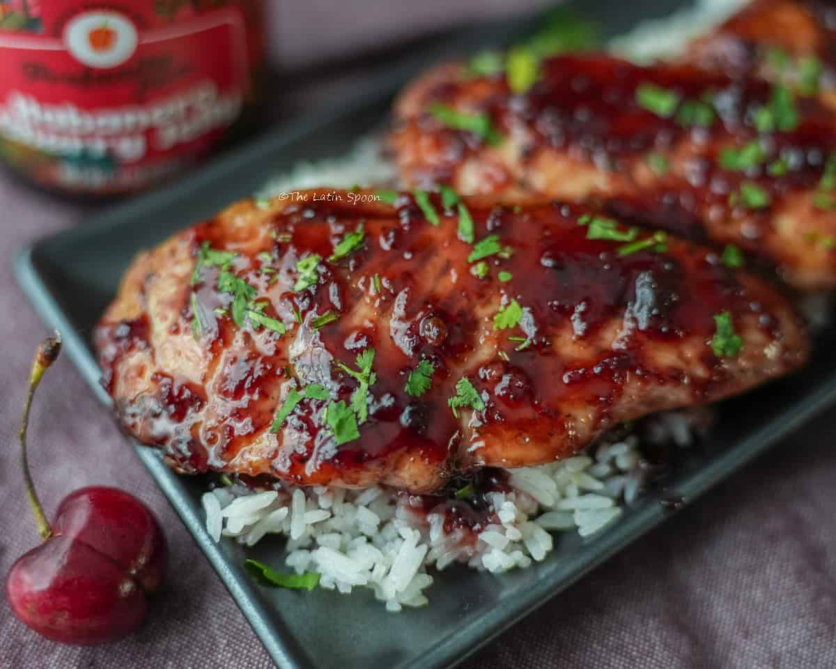 Un plato cuadrado negro, con una porcion de arroz blanco con dos pedazos de pollo con mermelada de cereza, la mermelada tiene un color oscuro