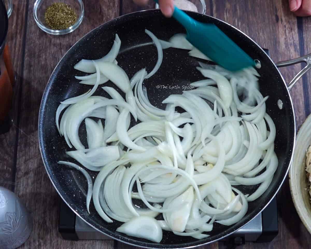 A skillet containing sliced onions being stirred with a spatula.