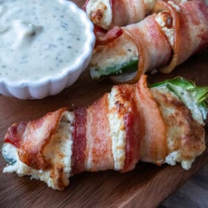 Bacon-wrapped stuffed jalapeños served next to a small bowl of ranch dressing.