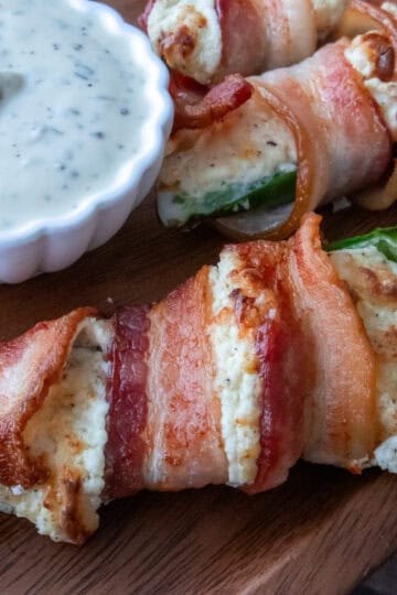 Bacon-wrapped stuffed jalapeños served next to a small bowl of ranch dressing.