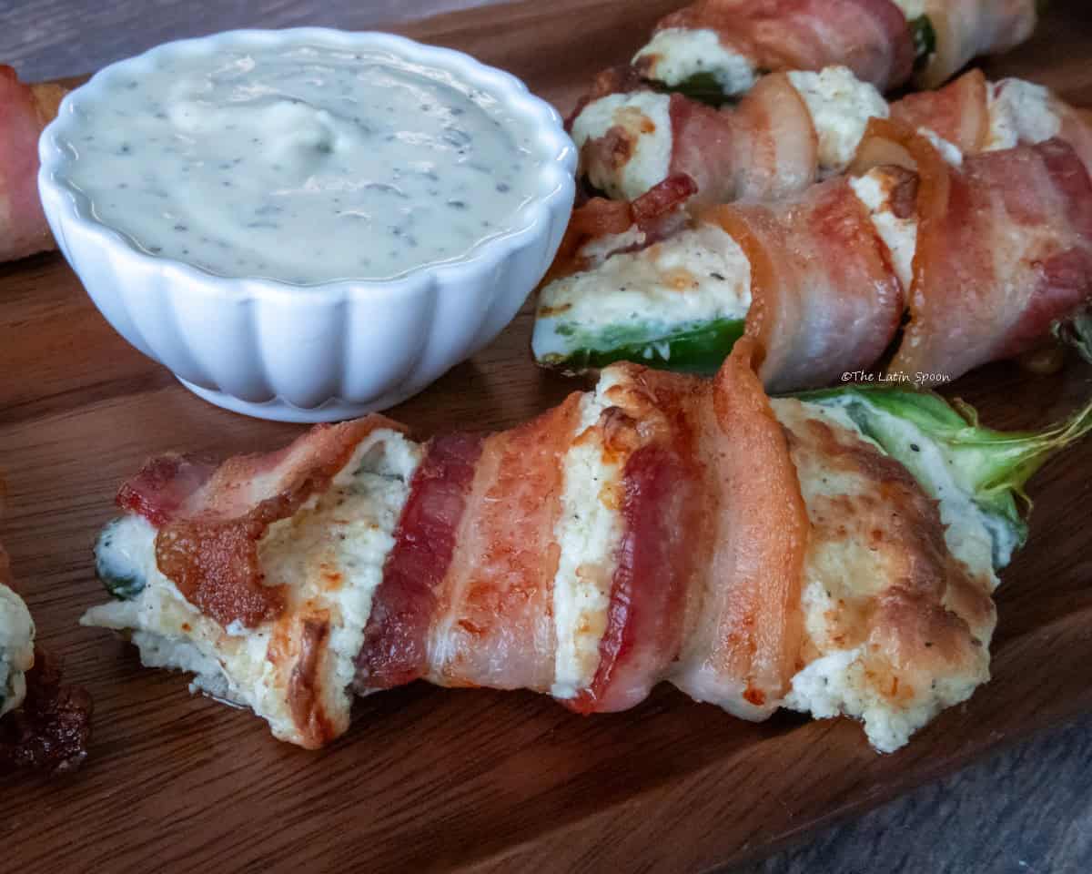 Bacon-wrapped stuffed jalapeños served next to a small bowl of ranch dressing.