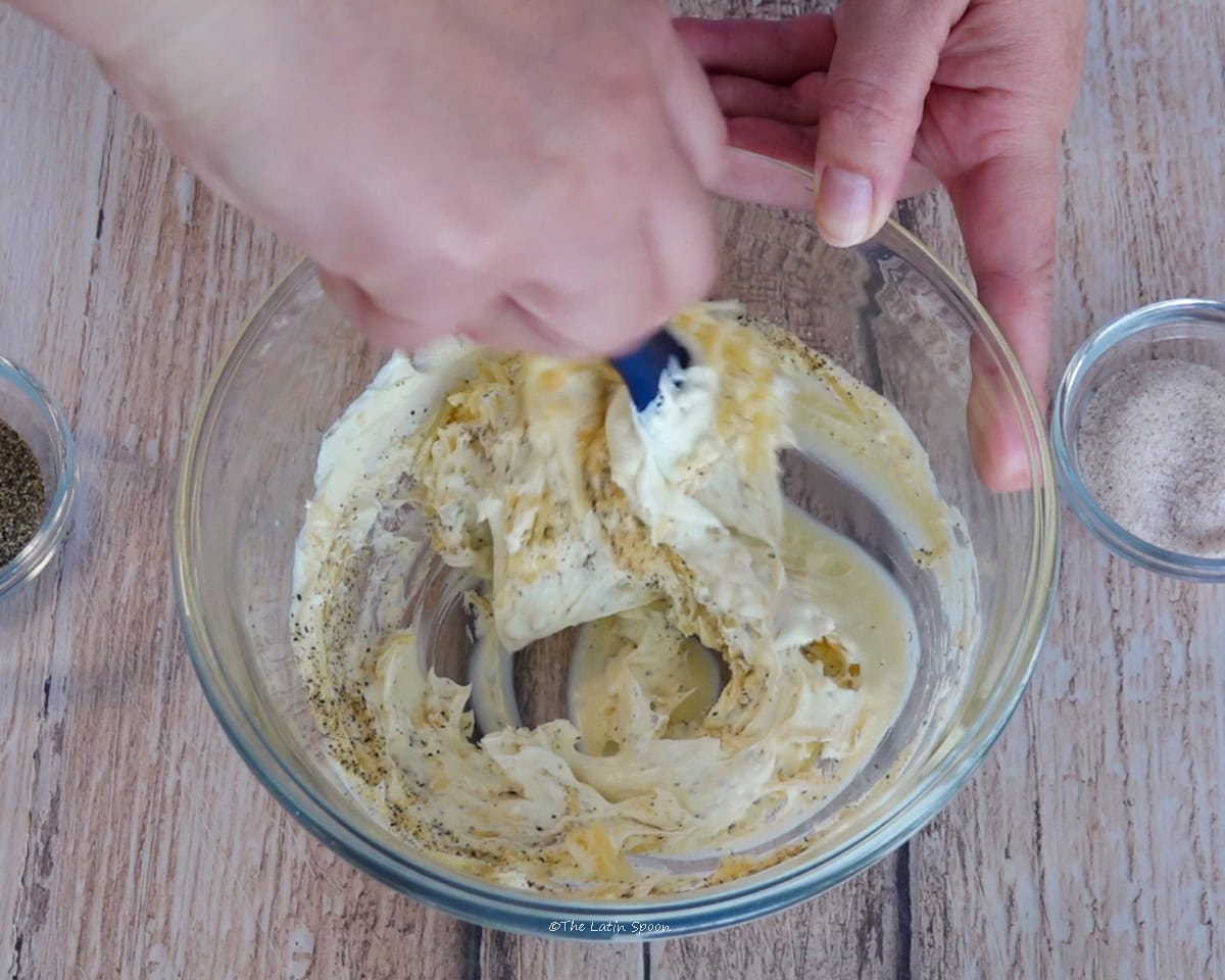 One hand holds the bowl while the other mixes the ingredients with a spatula.