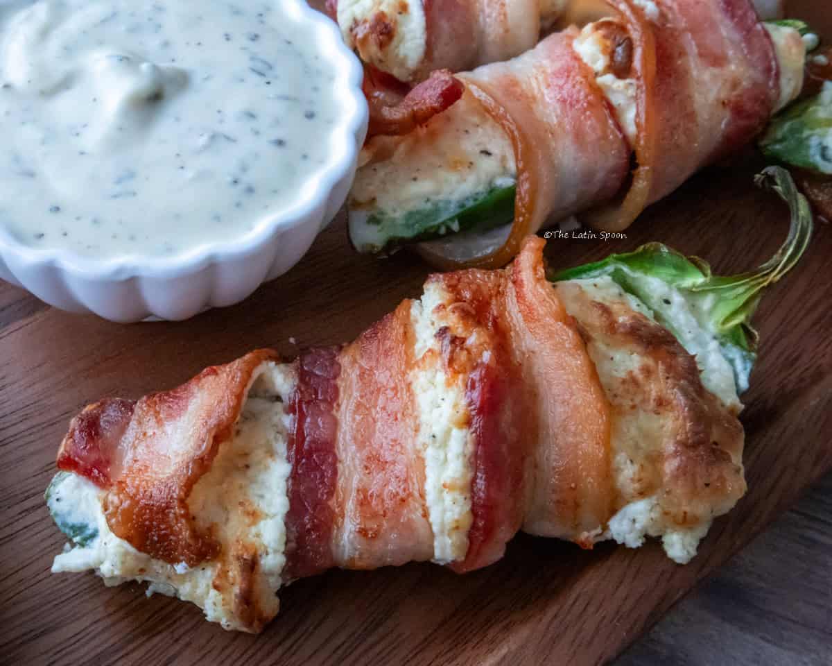 Bacon-wrapped stuffed jalapeños served next to a small bowl of ranch dressing.