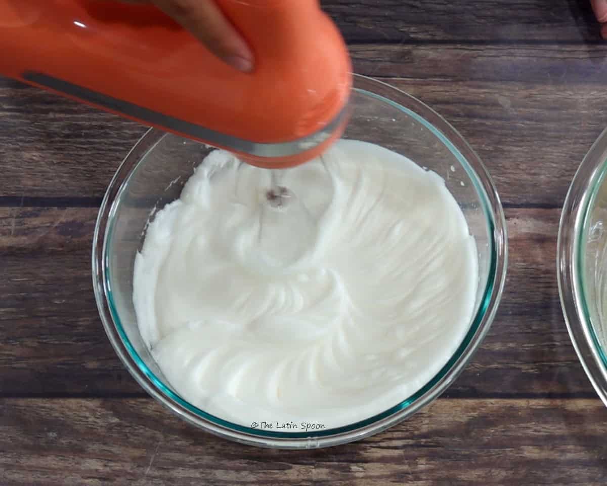 A bowl of beaten egg whites with a hand mixer inside.