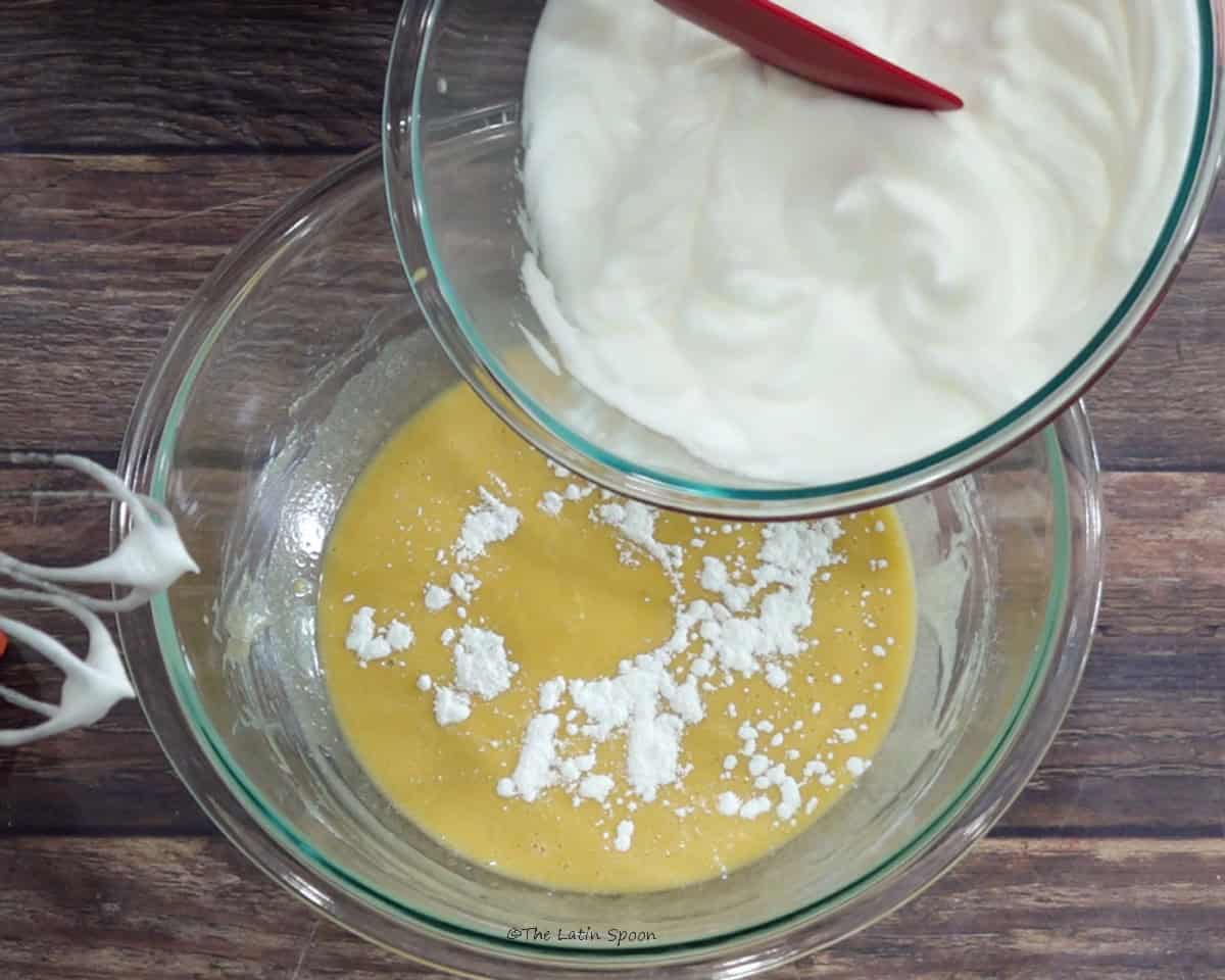 Beaten egg whites being added from one bowl to another bowl containing the beaten egg yolk mixture.