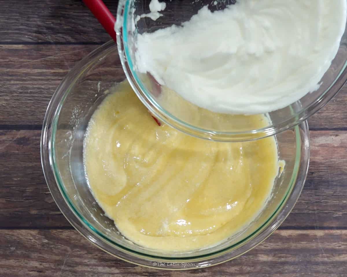 The remaining beaten egg whites being added from one bowl to another bowl containing the beaten egg yolk mixture.