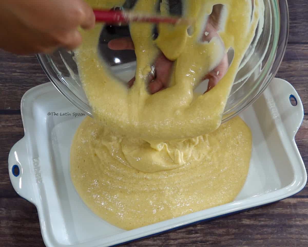 The batter is poured from a bowl into a baking dish with the help of a spatula.