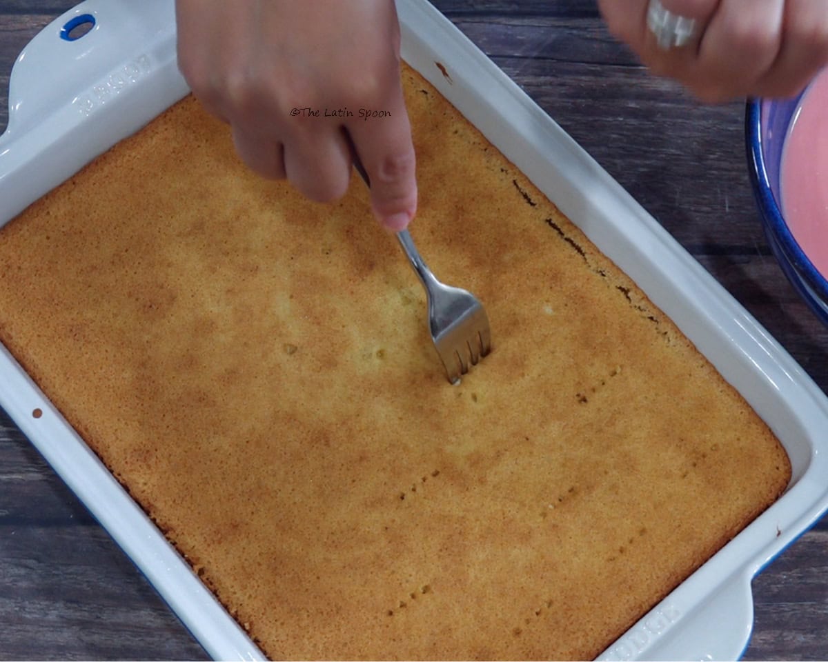 A baked cake in a glass baking dish being pierced with a fork.