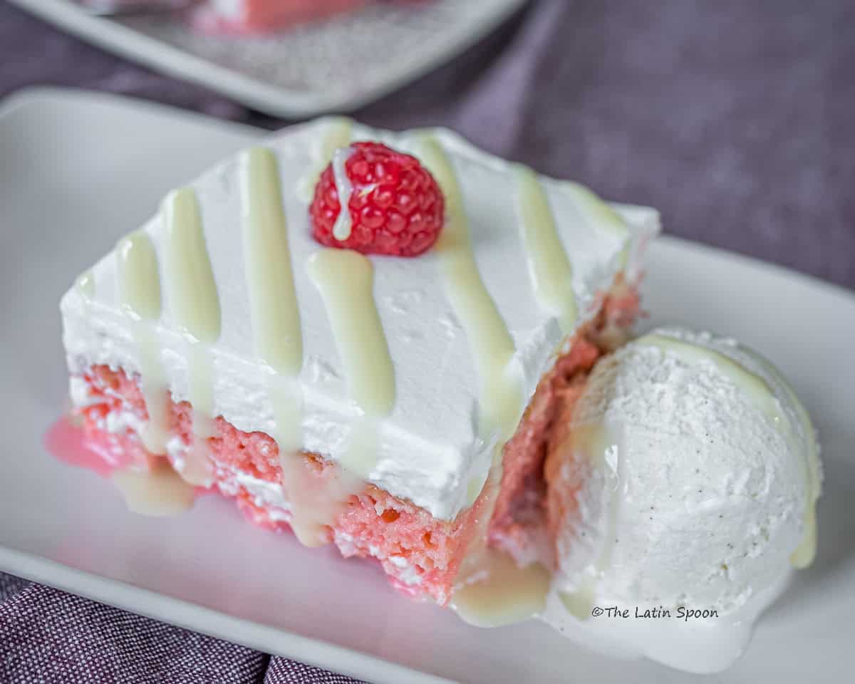 A square slice of Churchill tres leches cake served on a plate, drizzled with condensed milk and accompanied by a scoop of ice cream.