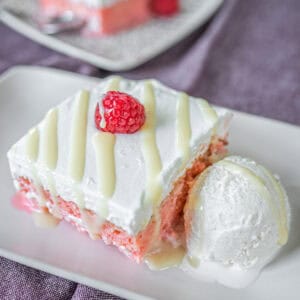 A square slice of Churchill tres leches cake served on a plate, drizzled with condensed milk and accompanied by a scoop of ice cream.