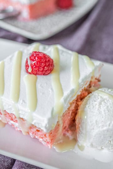 A square slice of Churchill tres leches cake served on a plate, drizzled with condensed milk and accompanied by a scoop of ice cream.