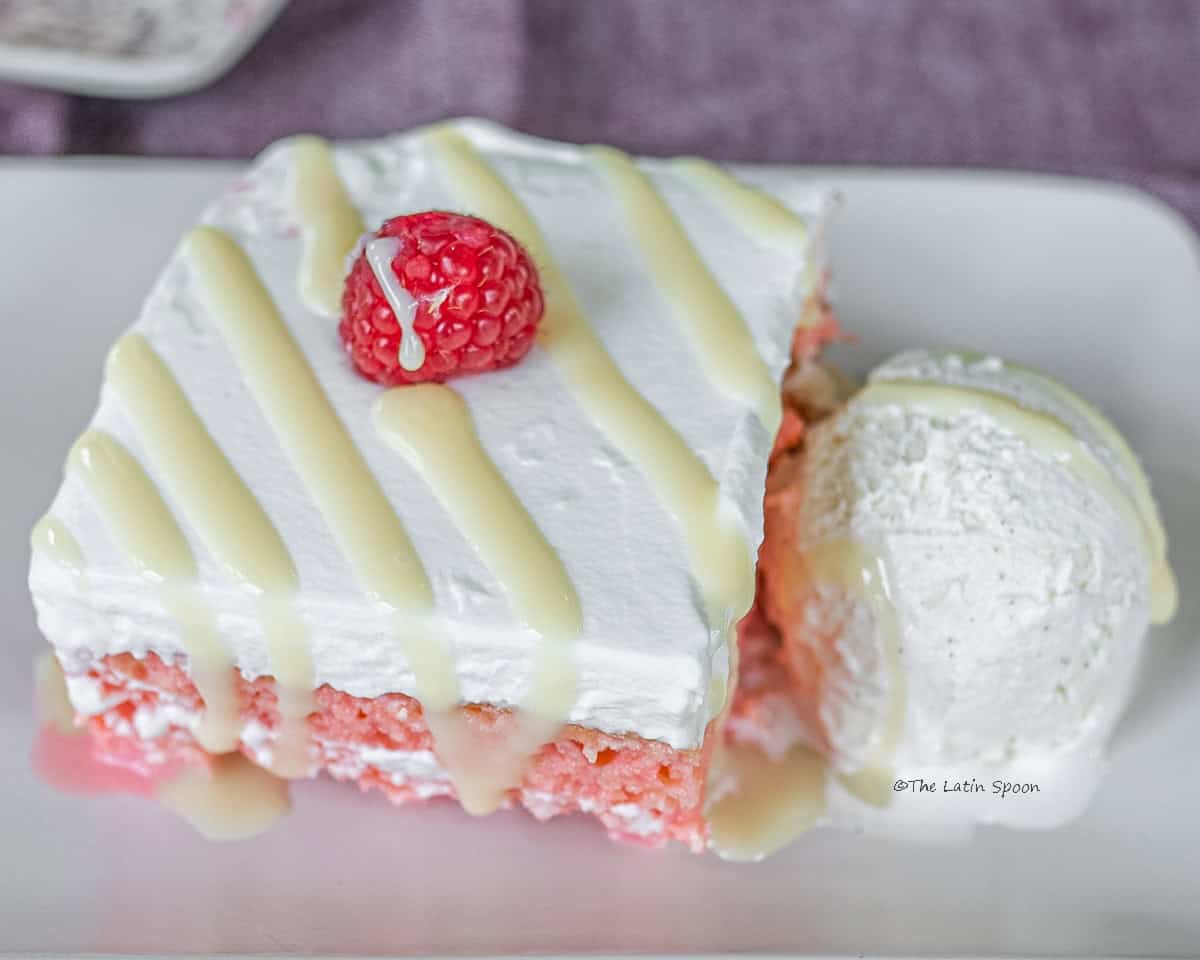 A square slice of Churchill tres leches cake served on a plate, drizzled with condensed milk and accompanied by a scoop of ice cream.