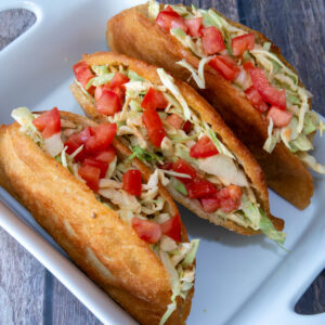 Three chicken empanadas opened along the side and filled with shredded cabbage and diced tomato, served with pink sauce on a white plate over a colorful tablecloth.