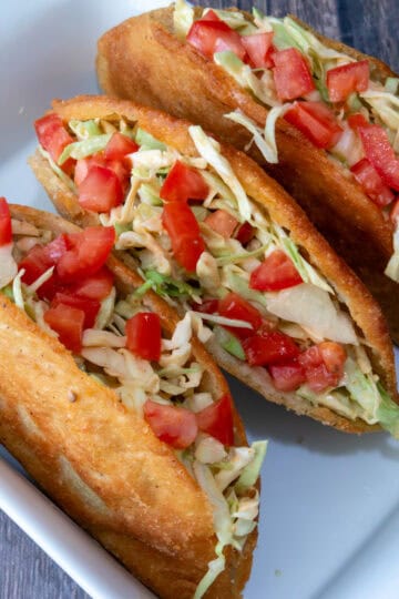 Three chicken empanadas opened along the side and filled with shredded cabbage and diced tomato, served with pink sauce on a white plate over a colorful tablecloth.