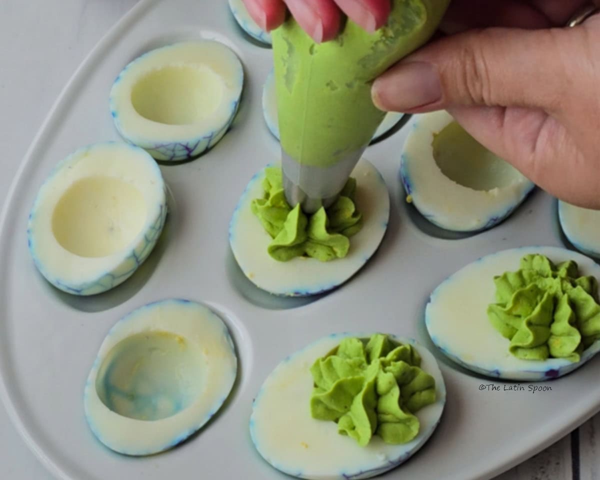 A plate of halved eggs being filled with the colored egg yolk mixture.