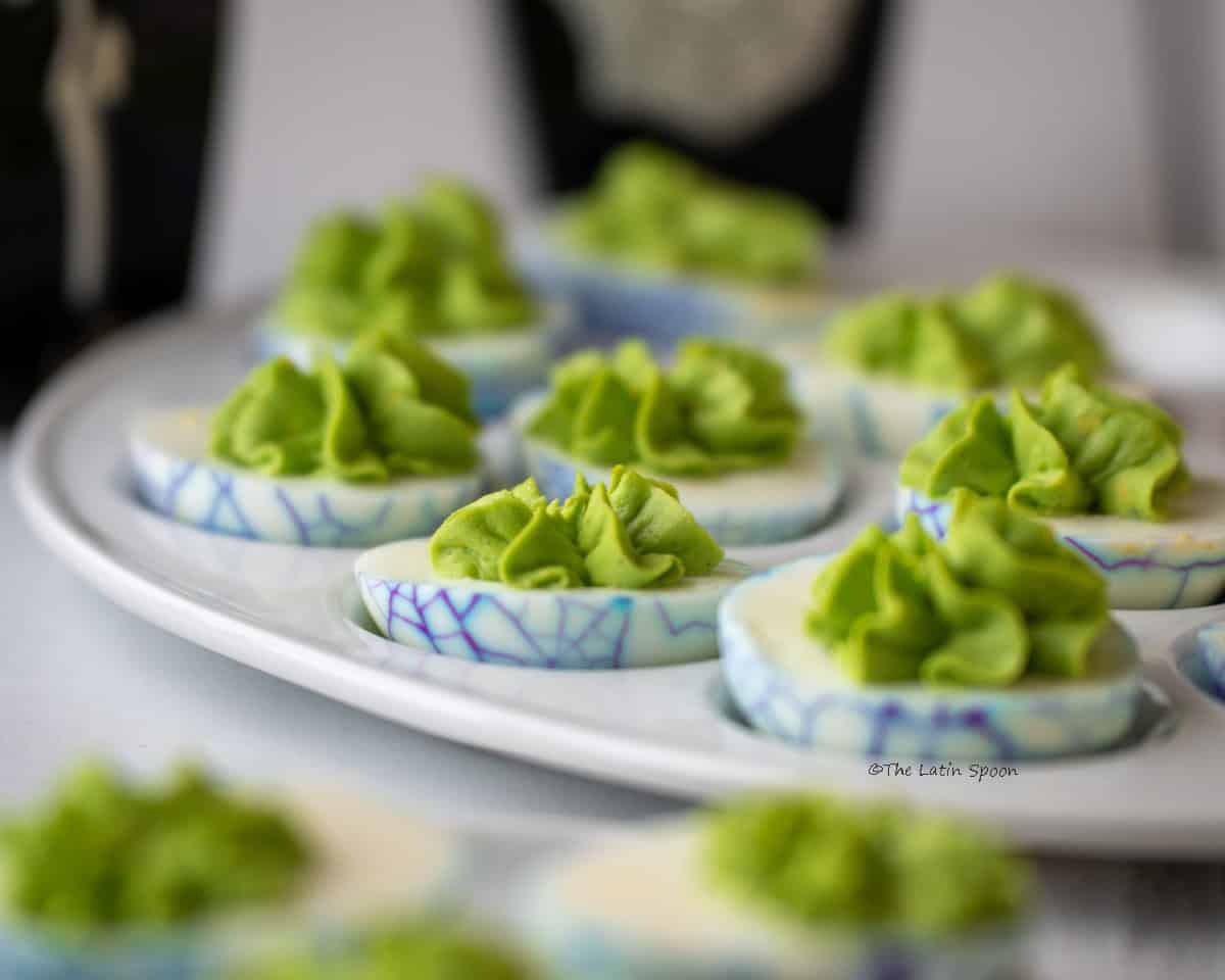 An egg-shaped serving platter containing deviled eggs with green-colored filling.