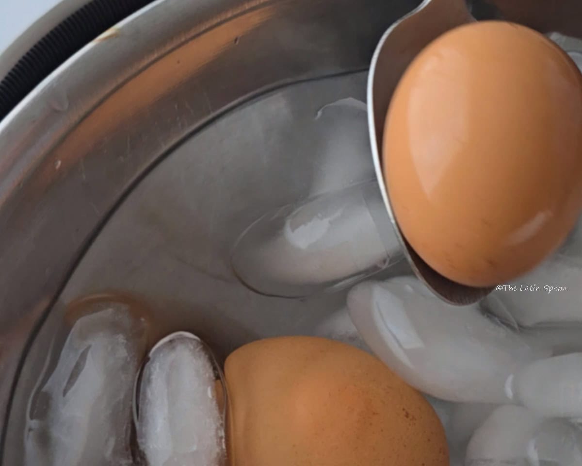 A bowl filled with ice water and eggs while a spoon removes them one at a time.