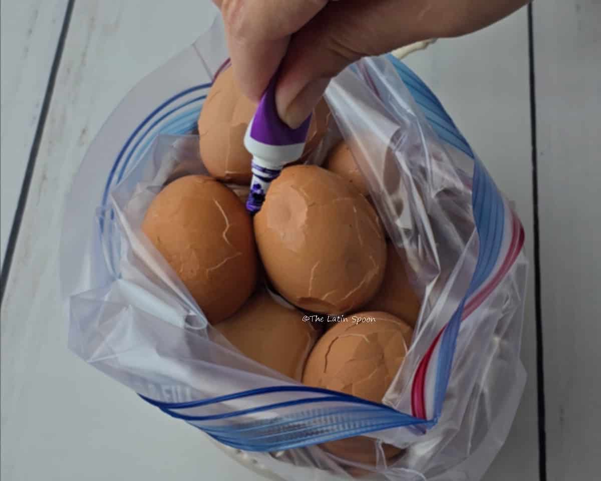A bag filled with crackled eggs while one hand adds food coloring to the water inside the bag.