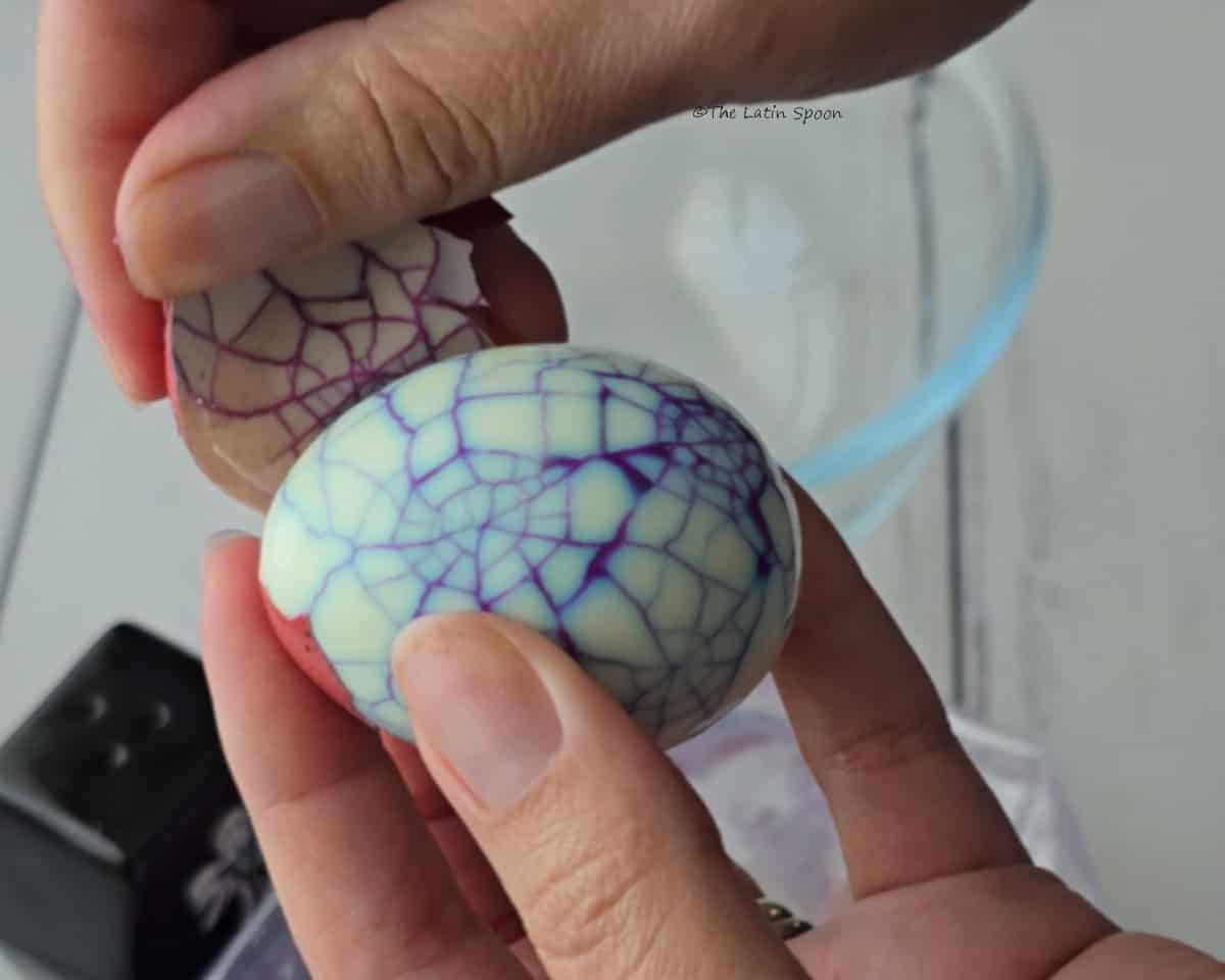 A bowl is visible in the background while two hands peel a cooked egg.